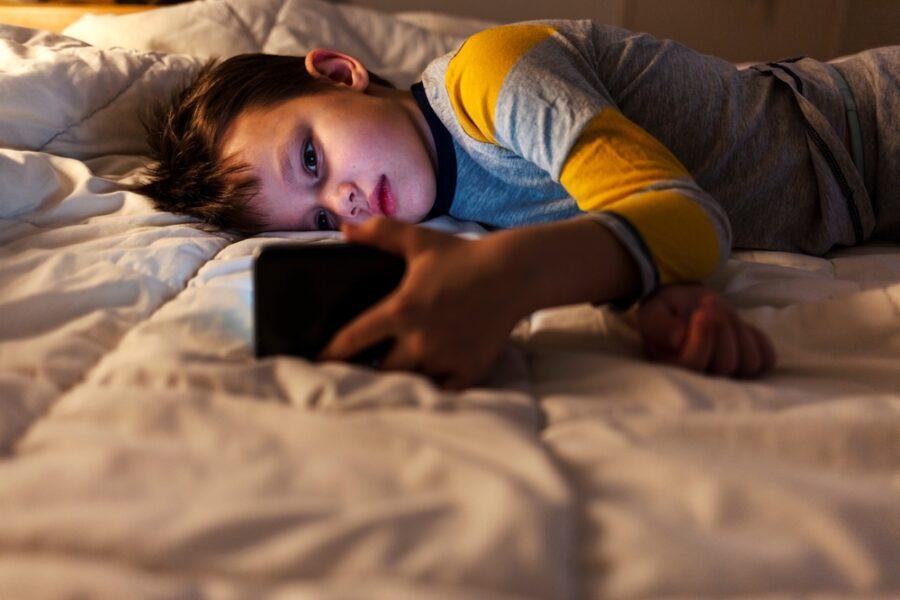 young,boy,laying,in,bed,and,watching,clips,by,smartphone.